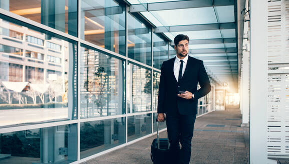 Gutaussehender junger Geschäftsmann, der vor einem Bahnhof für öffentliche Verkehrsmittel spazieren geht. Kaukasischer Geschäftsreisender mit Koffer am Flughafen. - JLPSF00847