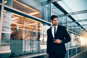 Handsome businessman walking with mobile phone. Businessman with cellphone in airport. - JLPSF00851