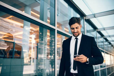 Geschäftsmann mit Smartphone und lächelnd am Flughafen. Junger Geschäftsmann mit Mobiltelefon am Flughafen. - JLPSF00855