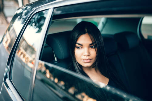 Schöne junge Geschäftsfrau, die auf dem Rücksitz eines Autos sitzt und aus dem Fenster schaut. Weibliche Geschäftsfrau, die mit einem Taxi unterwegs ist. - JLPSF00892