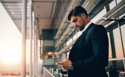 Seitenansicht eines jungen Geschäftsmannes, der auf dem Balkon der Flughafenlounge steht und ein Mobiltelefon benutzt. Ein Geschäftsmann wartet auf seinen Flug am Flughafen. - JLPSF00898