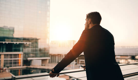 Rückansicht eines jungen Geschäftsmannes, der auf dem Balkon einer Flughafenlounge steht und nach draußen blickt. Ein Mann wartet im Flughafenterminal auf seinen Flug. - JLPSF00900