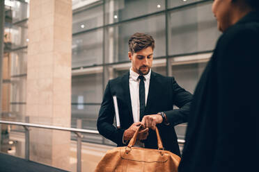 Junger Geschäftsmann am Flughafen mit Tasche, der auf seine Uhr schaut. Geschäftsreisender im Flughafenterminal, der die Zeit überprüft. - JLPSF00911