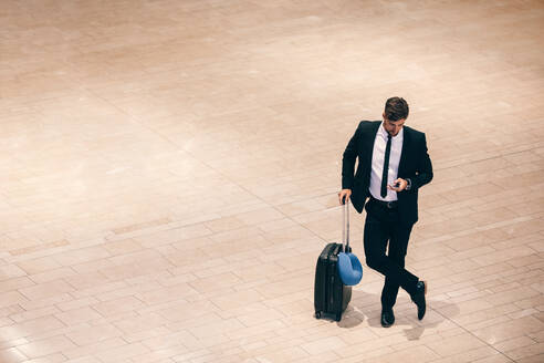 Top view shot of young businessman standing at airport terminal with suitcase and using mobile phone. business traveller reading text message cell phone while waiting for his flight. - JLPSF00920