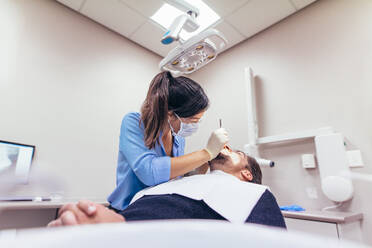 Female dentist examining a patient with tools in dental clinic. Doctor doing dental treatment on man's teeth in the dentists chair. - JLPSF00928