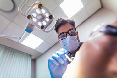 Stomatologe bei der Untersuchung der Mundhöhle eines Patienten in einer Zahnklinik. Männlicher Zahnarzt bei der Untersuchung der Zähne eines Patienten in seiner Praxis. - JLPSF00932