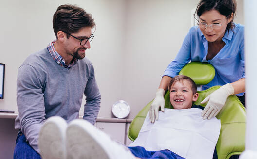 Lächelnder kleiner Junge sitzt auf dem Zahnarztstuhl in einer Zahnklinik mit Arzt und Krankenschwester. - JLPSF00934
