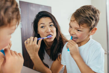 Mother and son brushing teeth in bathroom. Woman with her son brushing teeth together and looking in mirror. - JLPSF00947