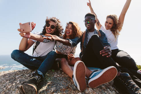 Freunde sitzen auf einem Berg und machen ein Selfie. Eine Gruppe von Männern und Frauen sitzt auf einem Hügel und macht ein Selfie. - JLPSF00952