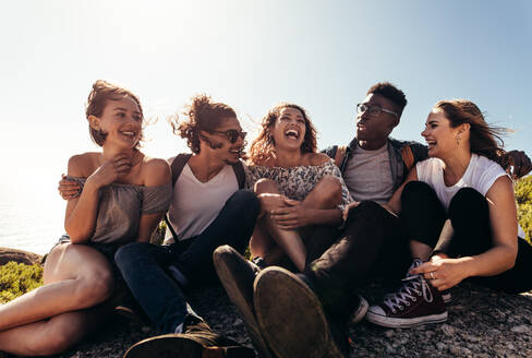 Eine Gruppe von Freunden, die auf einem Berggipfel zusammensitzen und sich amüsieren. Junge Männer und Frauen, die ihren Urlaub im Freien genießen. - JLPSF00965