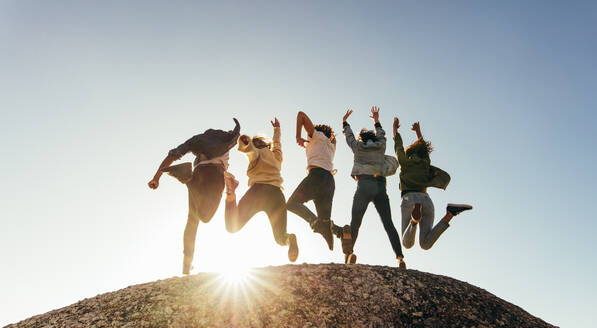 Rear view of group of happy friends having fun on mountain top. Men and women jumping on mountain top against sunset. - JLPSF00977