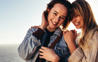 Close up of two young women standing outdoors and smiling. Cheerful female friends on holidays outdoors. - JLPSF00978