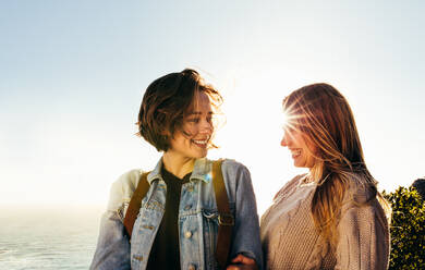 Two young women standing outdoors and looking at each other. Smiling female friends on summer holidays. - JLPSF00979