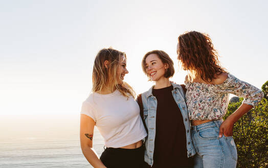Drei junge Frauen stehen im Freien und schauen sich an. Lächelnde Freundinnen, die sich im Sommerurlaub vergnügen. - JLPSF00980