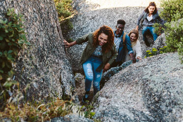 Junge Frau klettert auf Felsen mit Freunden im Hintergrund. Eine Gruppe von Freunden wandert durch einen Bergpfad. - JLPSF00982