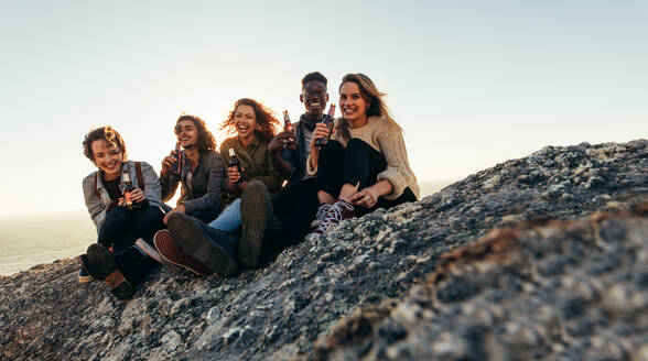 Eine Gruppe von Freunden sitzt auf einem Berggipfel und trinkt ein Bier. Fröhliche junge Männer und Frauen, die im Freien feiern und Spaß haben. - JLPSF00987