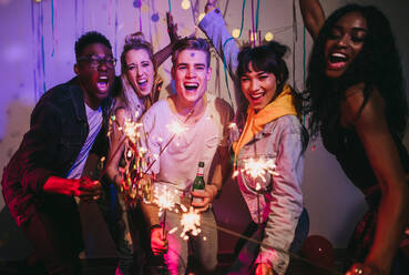 Friends celebrating with fire sparkles at a house party. Young men and women having fun at a colorful house party with decorations and confetti all around. - JLPSF00993