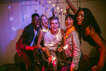 Friends celebrating with fire sparkles at a house party. Young men and women having fun at a colorful house party with decorations and confetti all around. - JLPSF00994