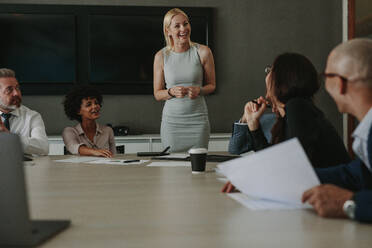 Eine Frau unterhält sich lächelnd mit einem Team von Geschäftsleuten im Sitzungssaal. - JLPSF01020