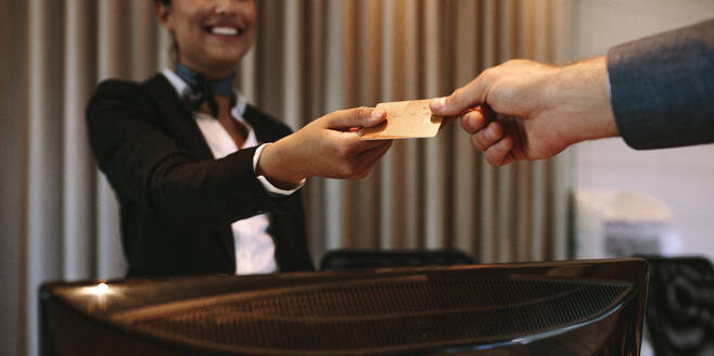 Nahaufnahme eines Geschäftsmannes, der mit einer Kreditkarte an der Rezeption eines Hotels bezahlt. Ein Geschäftsmann gibt der Rezeptionistin seine Kreditkarte, um sein Zimmer zu bezahlen. Fokus auf die Hände. - JLPSF01026