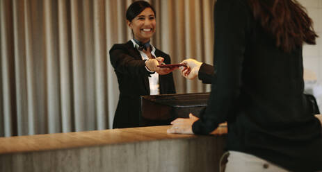 Lächelnde weibliche Concierge, die dem Hotelgast nach dem Einchecken die Dokumente zurückgibt. Weibliche Kundin, die ihre Dokumente an der Hotelrezeption nach dem Einchecken erhält. - JLPSF01027