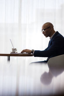 Männlicher Büroangestellter mit Laptop im Büro. Seitenansicht eines Geschäftsmannes, der am Tisch sitzt und am Laptop arbeitet. - JLPSF01043