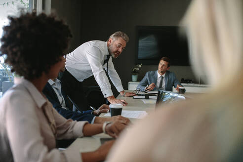 Ein leitender Angestellter, der seinem Team in einer Sitzung etwas erklärt. Geschäftsleute während einer Sitzung im Sitzungssaal. - JLPSF01046