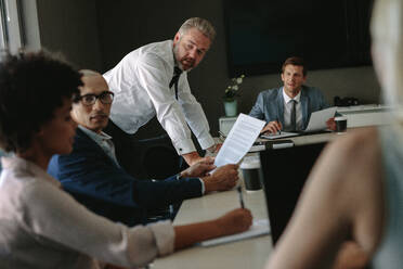 Multi-ethnic business team sitting at conference table and discussing new project. Senior executives working with young managers at office staff meeting. - JLPSF01048