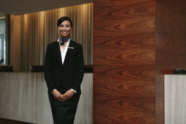Porträt einer glücklichen jungen Rezeptionistin, die an der Rezeption eines Hotels steht, um einen Gast zu begrüßen. Weibliche Concierge, die einen Gast im Hotel begrüßt. - JLPSF01064