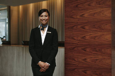 Porträt einer glücklichen weiblichen Hotelrezeptionistin, die am Arbeitsplatz steht. Lächelnde Frau an der Rezeption im Hotel. - JLPSF01065