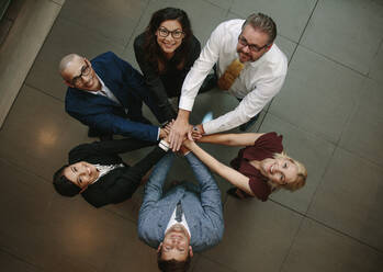 Top view of multi-ethnic business people putting their hands on top of each other and looking upwards. Business team making a stack of hands showing unity. - JLPSF01072