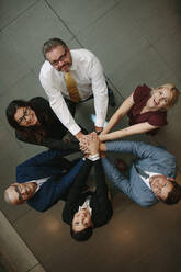 Overhead view of business people hands stacked together. Business team showing unity and looking up at camera. - JLPSF01073