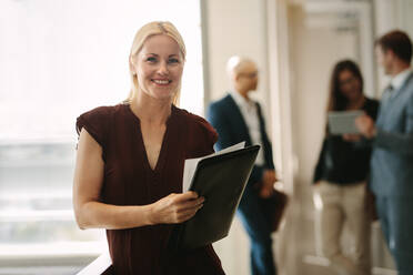 Happy business woman with coworkers talking in background. Female manager with colleagues at the back. - JLPSF01081