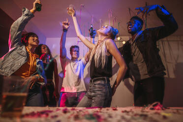 Young men and women having fun at a colorful house party. Friends dancing in joy holding drinks at a house party. - JLPSF01091