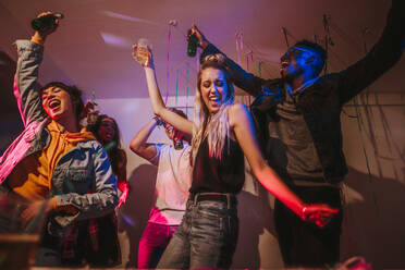 Young men and women having fun at a colorful house party. Friends dancing in joy holding drinks at a house party. - JLPSF01092