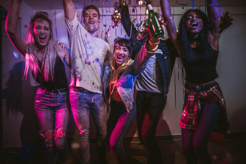 Young men and women having fun at a colorful house party with decorations and confetti all around. Friends dancing and celebrating holding drinks at a house party. - JLPSF01098