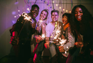 Friends celebrating with fire sparkles and drinks at a house party. Young men and women having fun at a colorful house party with decorations and confetti all around. - JLPSF01101