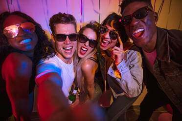 Friends posing for a selfie wearing dark sunglasses and making faces at a house party. Young men and women having fun at a colorful house party. - JLPSF01105