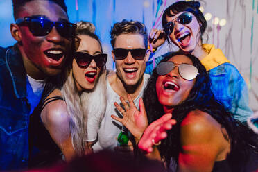 Freunde posieren für ein Selfie mit dunklen Sonnenbrillen auf einer Hausparty. Junge Männer und Frauen haben Spaß auf einer bunten Hausparty. - JLPSF01106
