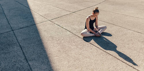 Ballet dancer stretching her legs before dance practice. Dancer sitting on floor joining both her feet. - JLPSF01125
