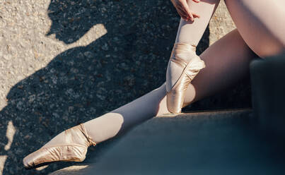 Closeup of ballet dancer sitting outdoors. Ballet dancer wearing pointe shoes sitting on stairs. - JLPSF01137