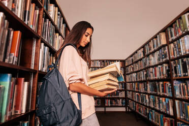 Young female student carrying lots of books in the college library. Caucasian student reading books in library. - JLPSF01153