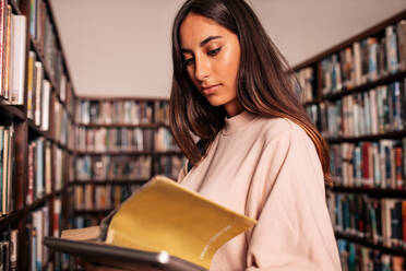 Studentin liest Buch mit Tablet in der Bibliothek. Junge Studentin studiert in Buch in Bibliothek. - JLPSF01155