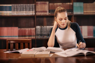 College student preparing for the exam in library. University student taking notes from book while sitting in library. - JLPSF01159