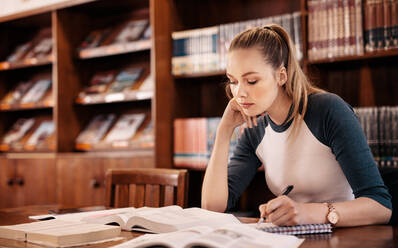 Junger kaukasischer Student, der in der Bibliothek aus einem Buch lernt. College-Student, der in der Bibliothek Notizen für eine Prüfung macht. - JLPSF01160