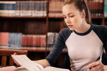 Junge Studentin, die in der Bibliothek aus einem Buch lernt. Studentin, die in der Bibliothek Notizen für die Prüfung vorbereitet. - JLPSF01162