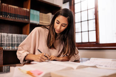 Young student making notes in the library. College female student preparing for the exam while sitting in library. - JLPSF01166