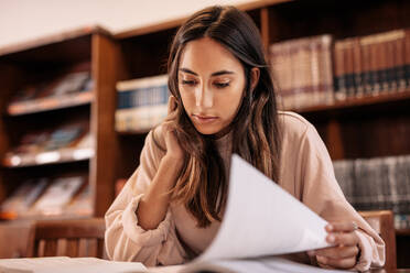 Junge Studentin beim Lesen von Nachschlagewerken in der öffentlichen Bibliothek. Studentin bei der Recherche mit einem Buch in der Bibliothek. - JLPSF01168