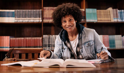Junge selbstbewusste Studentin, die in der Bibliothek aus Büchern lernt. Universitätsstudentin, die in der Bibliothek studiert. - JLPSF01175