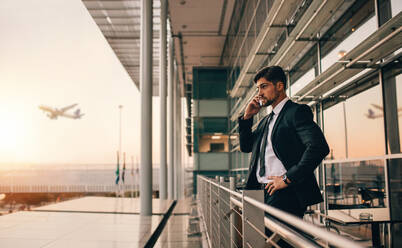 Seitenansicht eines jungen Geschäftsmannes, der auf dem Balkon der Flughafenlounge steht und mit seinem Handy spricht. Ein gutaussehender kaukasischer Mann wartet auf seinen Flug. - JLPSF01179